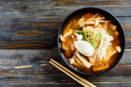 Kimchi soup with mushroom in a bowl and chopsticks on wooden background, Korean food, top view